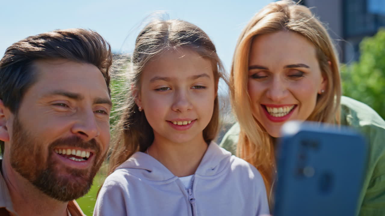 Nahaufnahme eines positiven Familien-Videoanrufs über ein Mobiltelefon beim Picknick auf grünem Gras