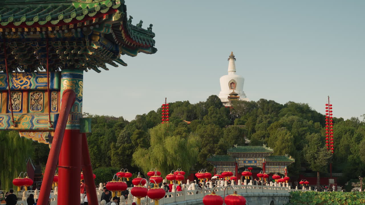 Pagoda bianca sopra un padiglione del tempio, folla asiatica che celebra il festival delle lanterne tra colonne rosse ornate e tetti intagliati, turisti che fotografano, venditori di snack, luce solare estiva, verde lussureggiante