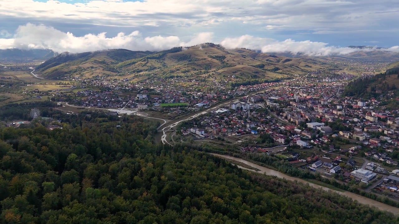 Prospettiva drone della città di Gura Humorului in una giornata di sole, circondata da colline coperte di alberi e vegetazione.
