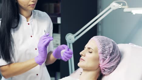 beautiful doctor softly pricking female's face. portrait of young woman receiving hyaluronic acid injection in forehead