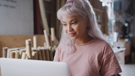 Young-Female-Business-Owner-In-Workshop-For-Sustainable-Bicycles-Doing-Accounts-On-Laptop