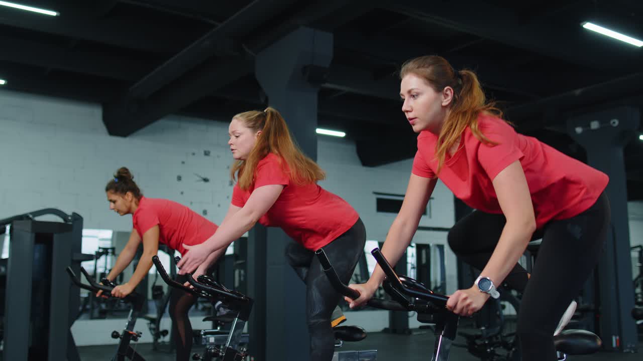 Group of smiling friends women class exercising training spinning on stationary bike at modern gym