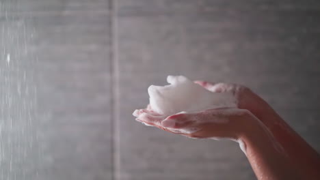 las manos de la mujer sostienen la espuma soplada de las palmas en el primer plano de la cabina de ducha. la dama juega con espuma esponjosa mientras se baña en el baño de la casa. producto cosmético higiénico