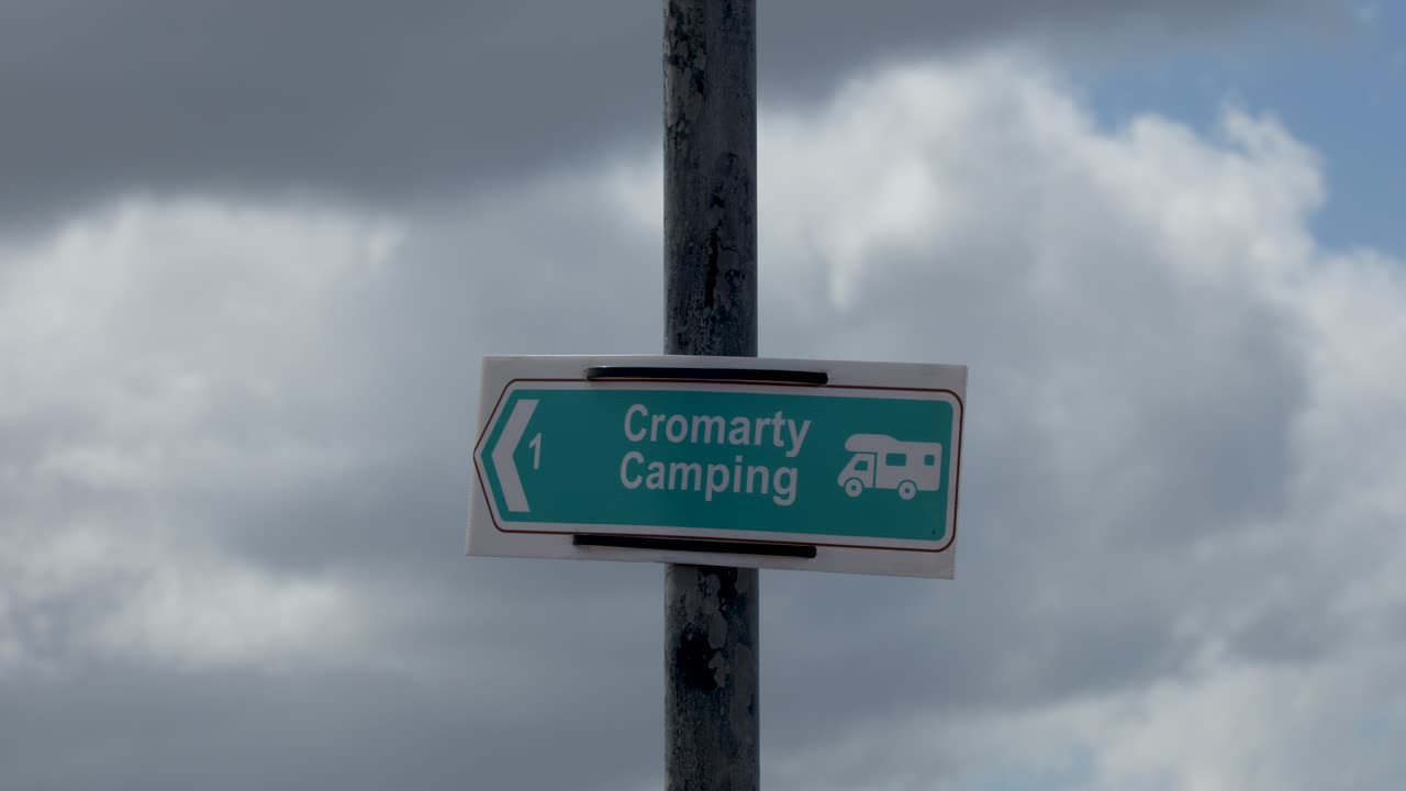 Green Cromarty Camping sign with arrow, roadside, cloudy sky, slight camera movement, overcast lighting