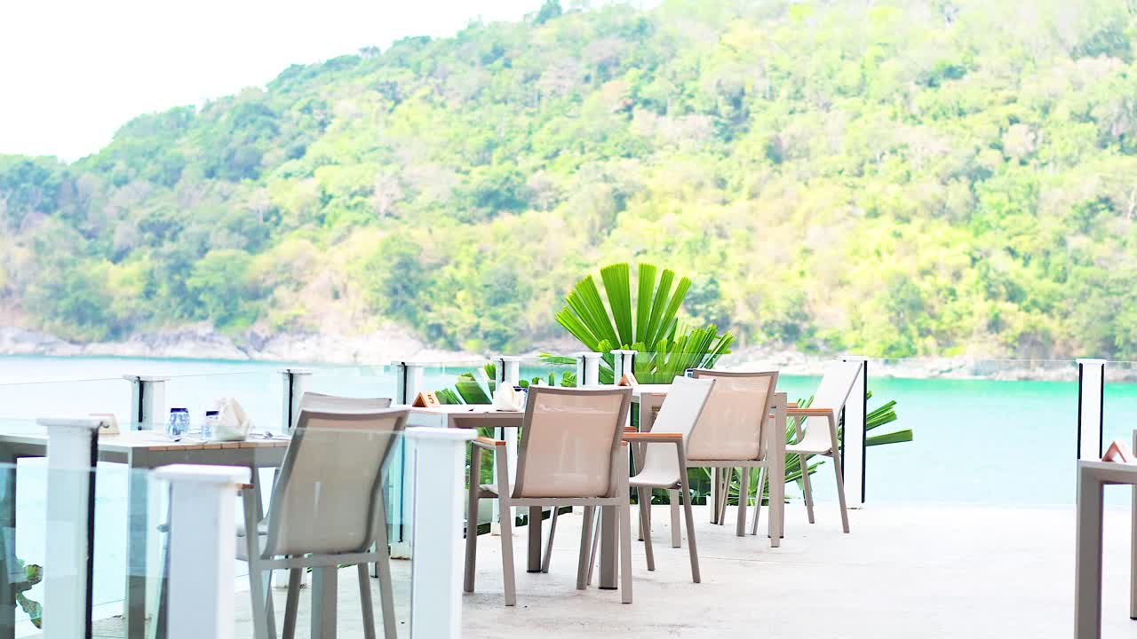 Outdoor dining setup with elegant tables and chairs, surrounded by lush greenery and a tranquil sea view in Phuket, Thailand