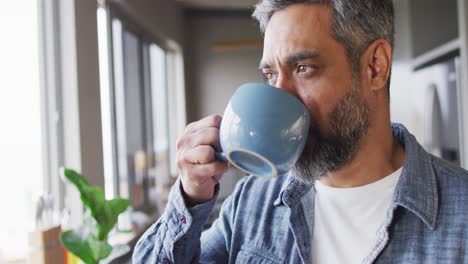 hombre biracial bebiendo taza de café y pensando solo en la cocina
