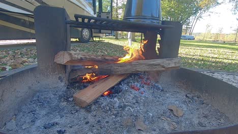 bucle: tres troncos ardiendo en un anillo de fogata en un campamento con una cafetera antigua que se alza sobre las brasas