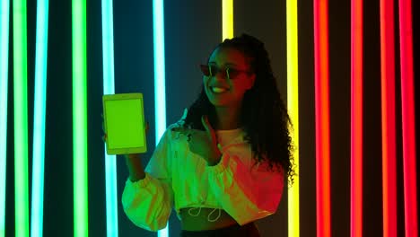 retrato de una joven y encantadora mujer afroamericana señala con el dedo el teléfono inteligente con la tecla de croma de pantalla verde, haciendo el gesto de la roca y los pulgares hacia arriba.