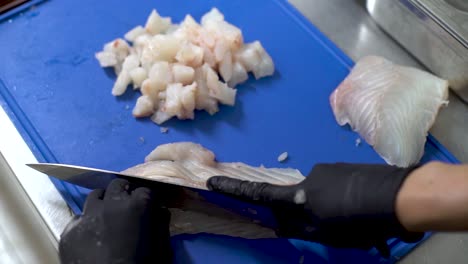 chef hands with black gloves cutting fish on a blue cutting board