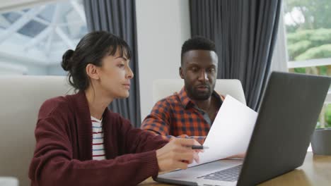 pareja feliz y diversa sentada a la mesa y trabajando con una computadora portátil