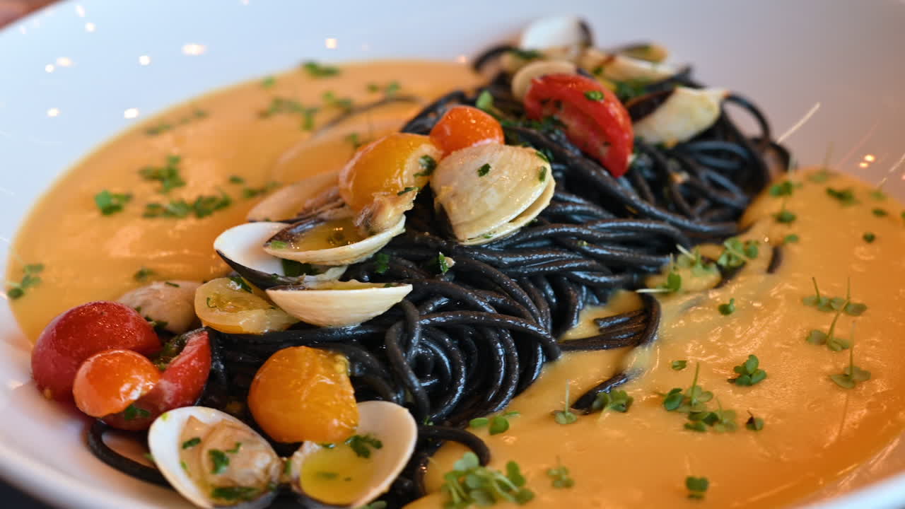 Spaghetti neri con vongole e salsa di pomodoro su un piatto bianco