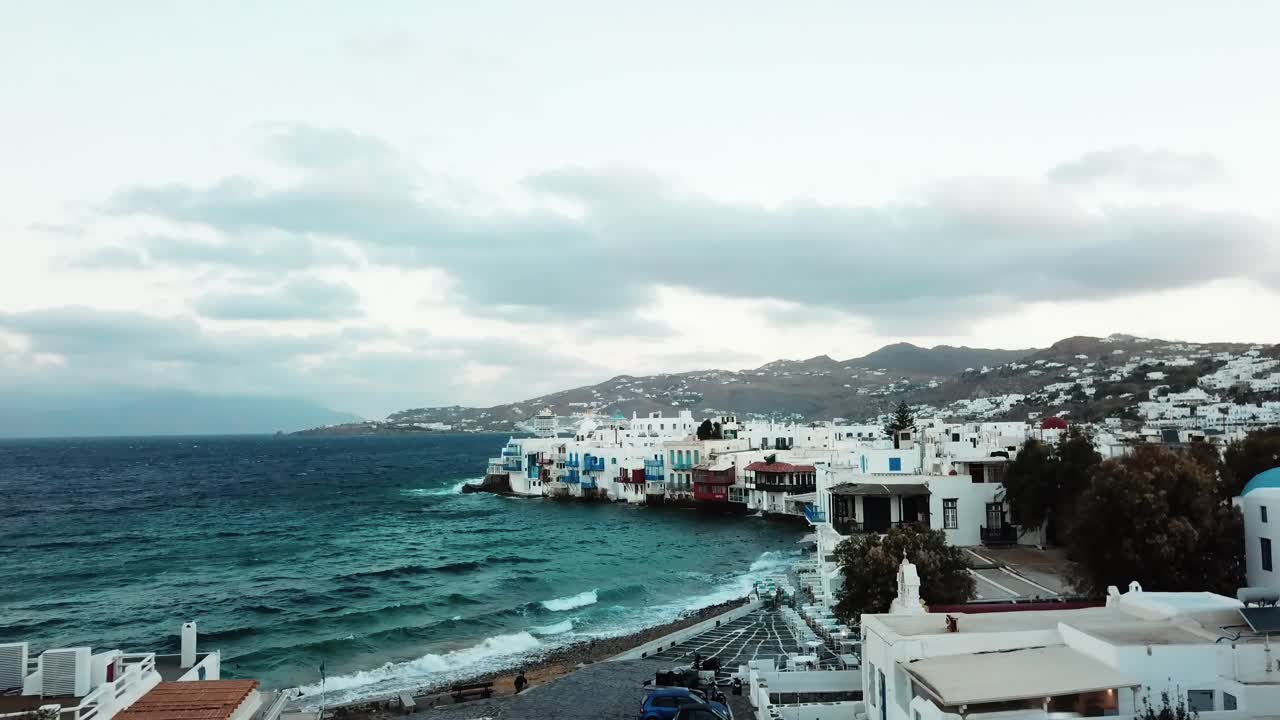 vista aérea de drones de olas de agua claras que tocan la costa con hermosas casas blancas en la costa de mykonos en grecia en un día nublado y soleado
