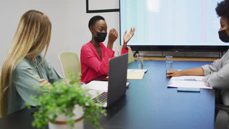 Tres-Empresarias-Diversas-Que-Usan-Máscaras-Faciales-En-Una-Discusión-En-Una-Reunión-De-Oficina