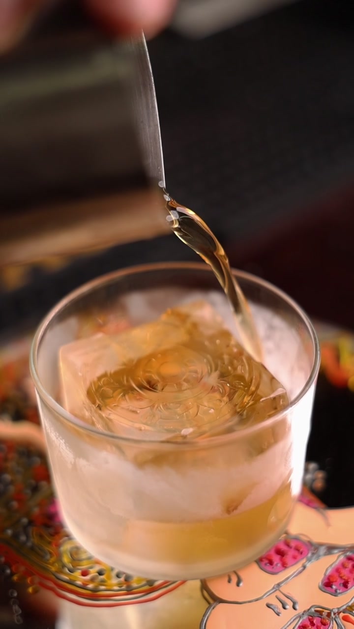 Bartender vertendo coquetel âmbar sobre um grande cubo de gelo decorativo
