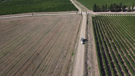 Agricultural-tractor-moving-between-neighboring-wheat-and-vineyard-fields-in-small-town-near-Tuscany-,-Italy