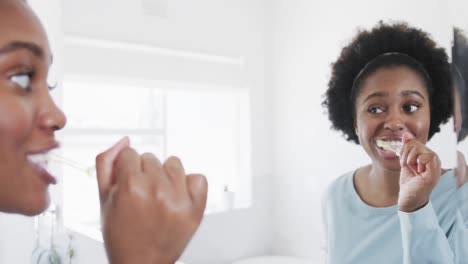 african american woman brushing teeth and looking in bathroom mirror, slow motion