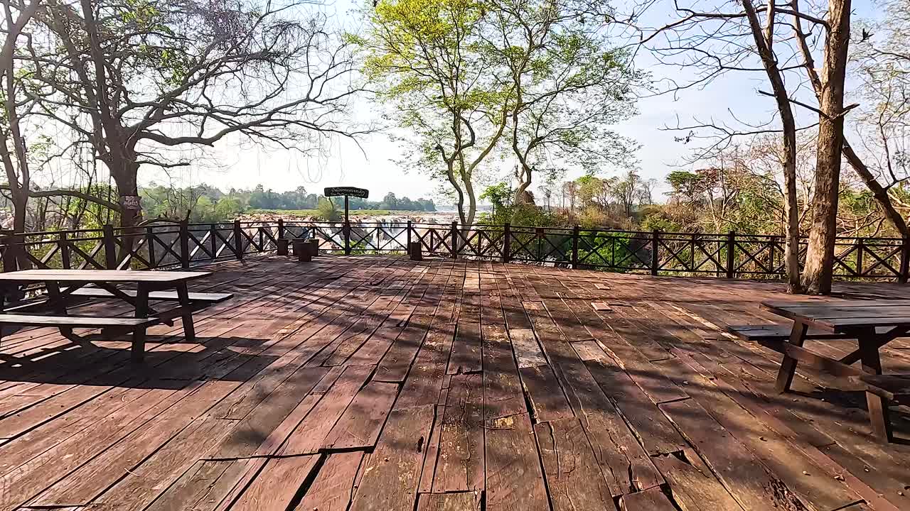 A serene wooden deck with benches overlooks lush greenery and distant views in Geelong, Australia. Bright daylight enhances the tranquil setting