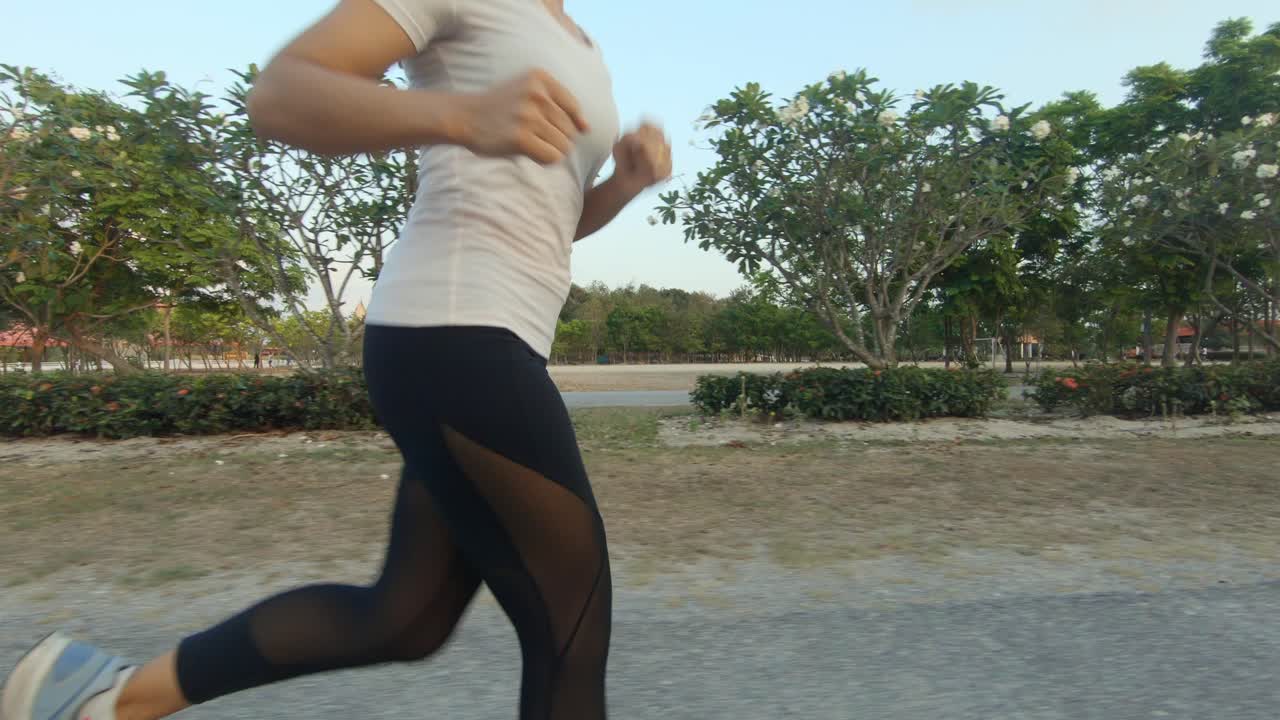A slowmotion side shot of a young thai girl jogging through a park