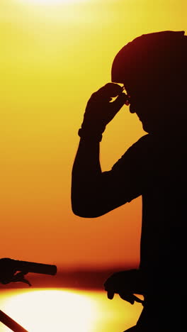professional cyclist takes off his protective glasses while standing at a beautiful sunset. silhouette of a sporty cyclist in helmet on a bike taking down glasses at golden color of sun setting. vertical video