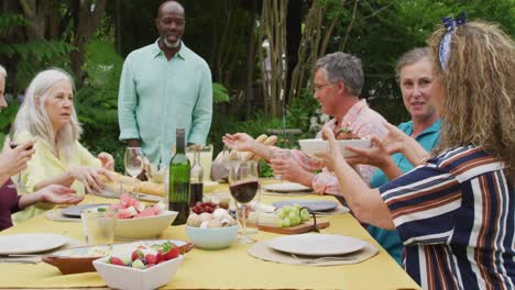 Animation-of-happy-diverse-female-and-male-senior-friends-having-lunch-in-garden