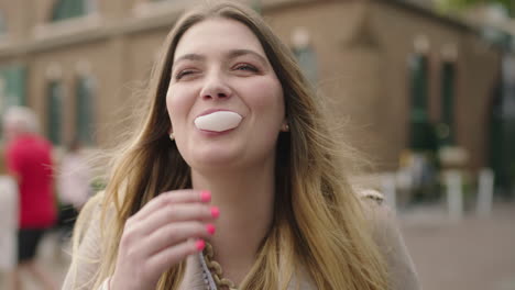 portrait-of-young-happy-blonde-woman-blowing-bubblegum-laughing-optimistic-on-urban-background