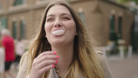 portrait of young happy blonde woman blowing bubblegum laughing optimistic on urban background