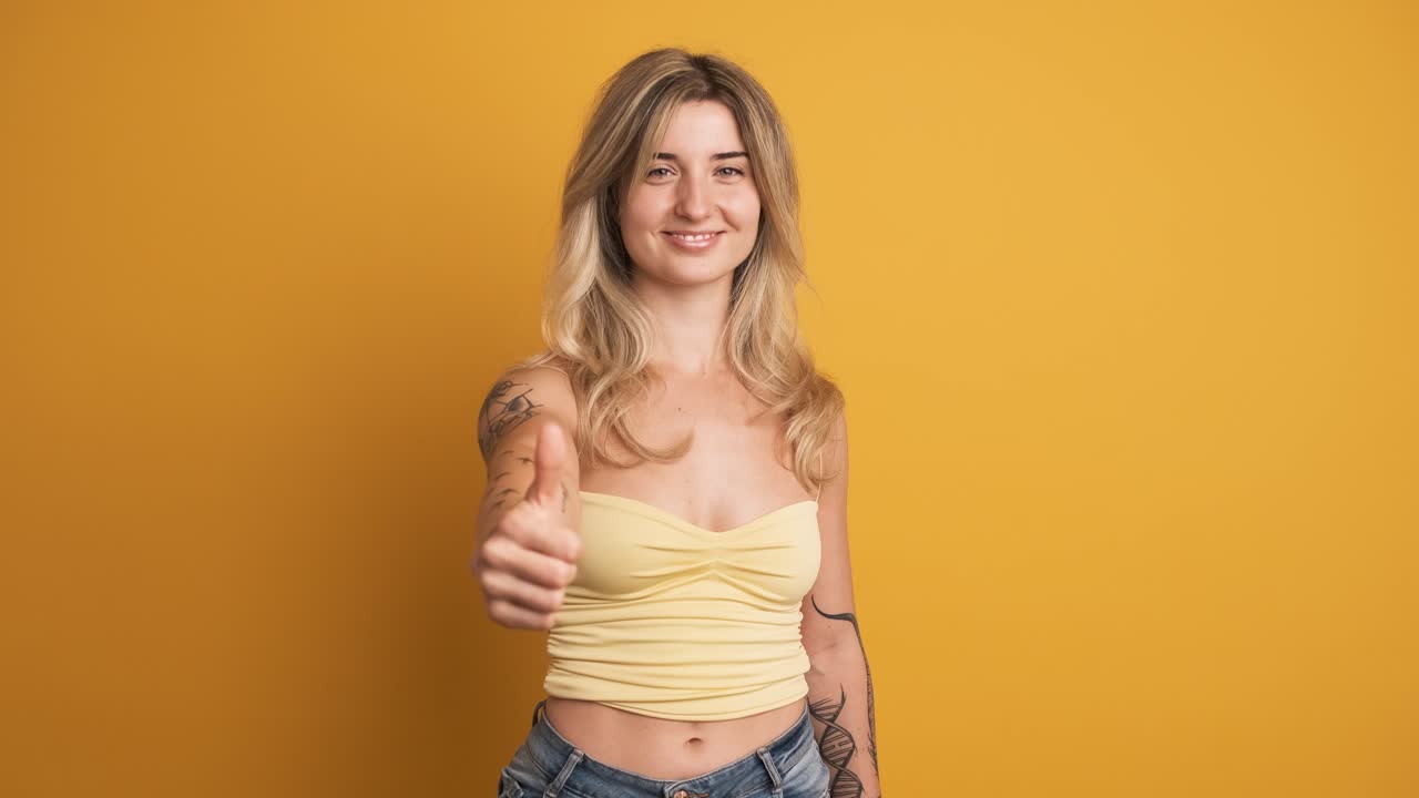 Happy young woman showing thumb up gesture on yellow background