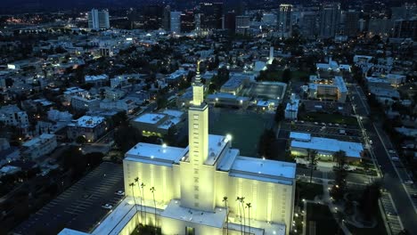 Aerial-orbit-of-LDS-Church,-Los-Angeles-California-Temple-during-blue-night-hour-overlooking-city