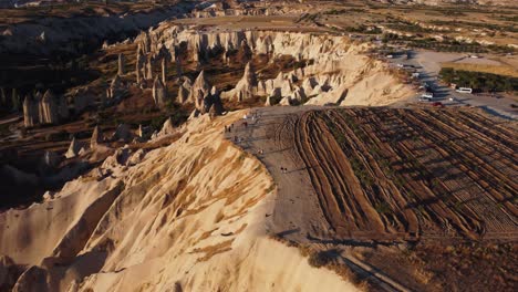 Drone-shot-of-Love-Valley-in-Cappadocia-with-visible-fields-hot-air-balloons-Fairy-Chimneys-rock-formation-and-people-on-the-edge-of-the-cliff