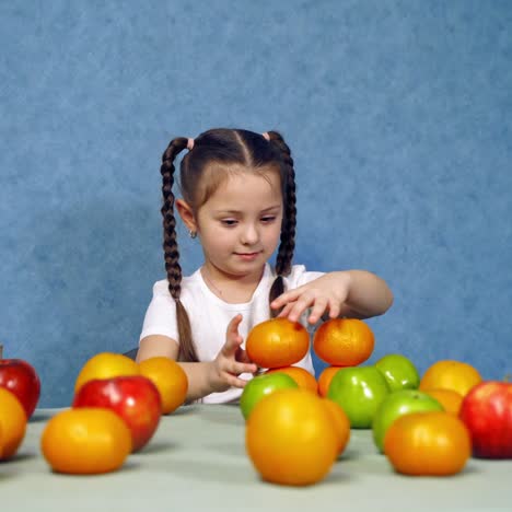 cute small girl with fruit at home. little child is building a tower of fresh fruits on the table. happy kid with organic healthy food.