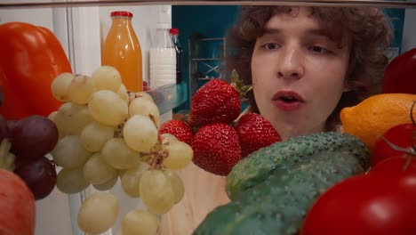 person looking inside open refrigerator filled with fruits and vegetables