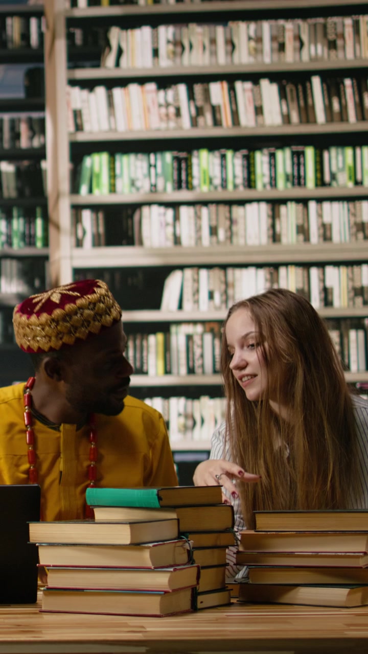 Video verticale: Gruppo di studio in biblioteca che discute idee attorno a un laptop e libri impilati