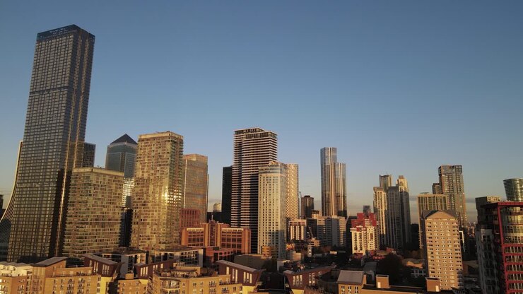 Carrello aereo di grattacieli illuminati d'oro nel quartiere di Canary Wharf a Londra durante il tramonto.