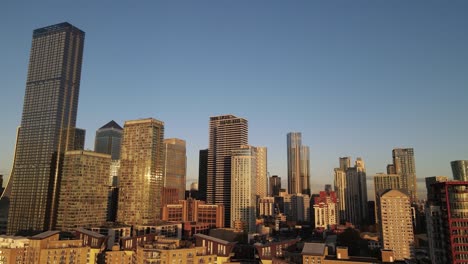 aerial trucking shot of golden lighting skyscraper buildings of canary wharf district in london during sunset