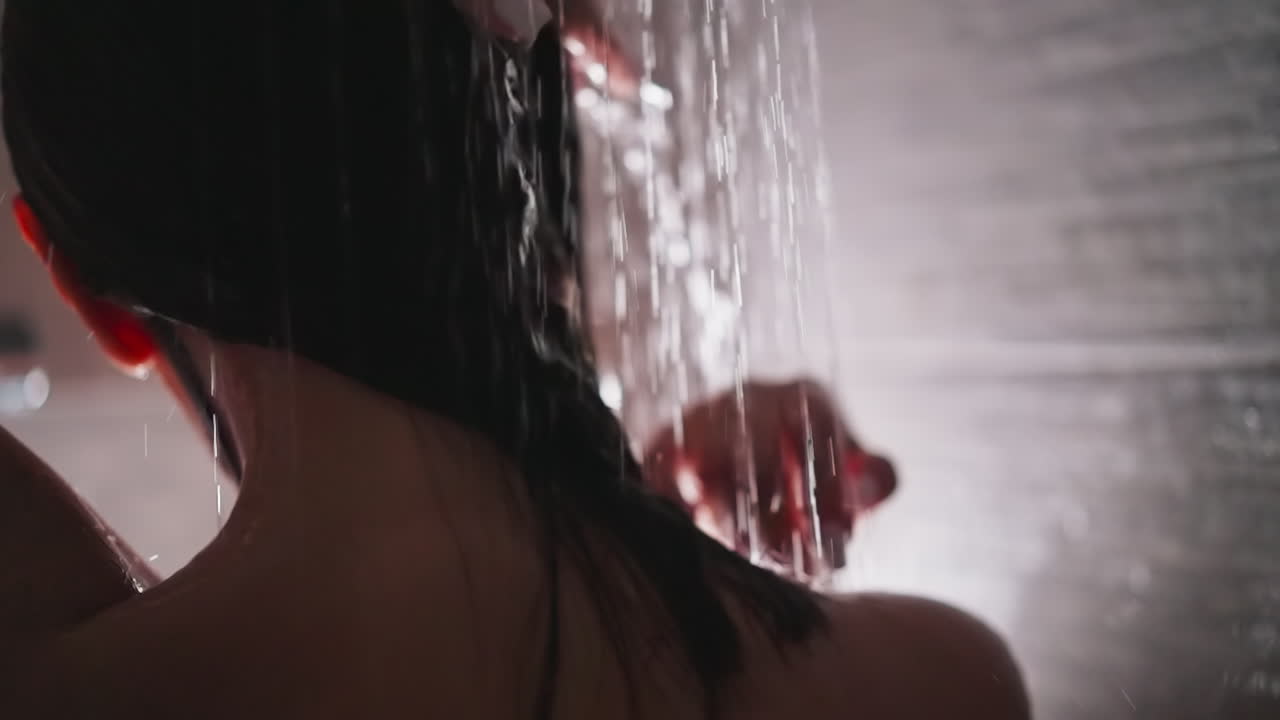 mujer disfruta de lavarse el cabello en la unidad de ducha de primer plano. dama graciosa ajusta el cabello de pie bajo chorros de agua caliente en el baño. concepto de higiene y belleza