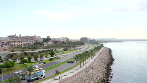 AERIAL:-Coast-road-with-cars,-traffic-on-ocean-with-Palm-trees-on-Tropical-Island-Mallorca,-Spain-on-Sunny-Day-Vacation,-Travel,-Sunny