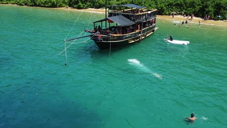 girl diving off of a pirate ship set anchor off coast of island in crystal clear water in brazilian ocean