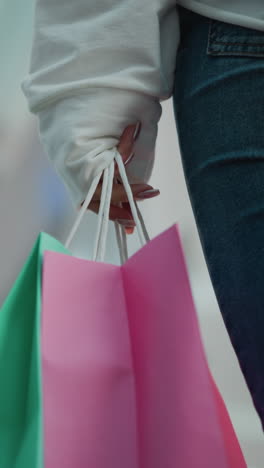 primer plano de bolsas de compras verdes y rosas sostenidas por una mujer caminando en un centro comercial moderno con iluminación vibrante borrosa y fondo dinámico