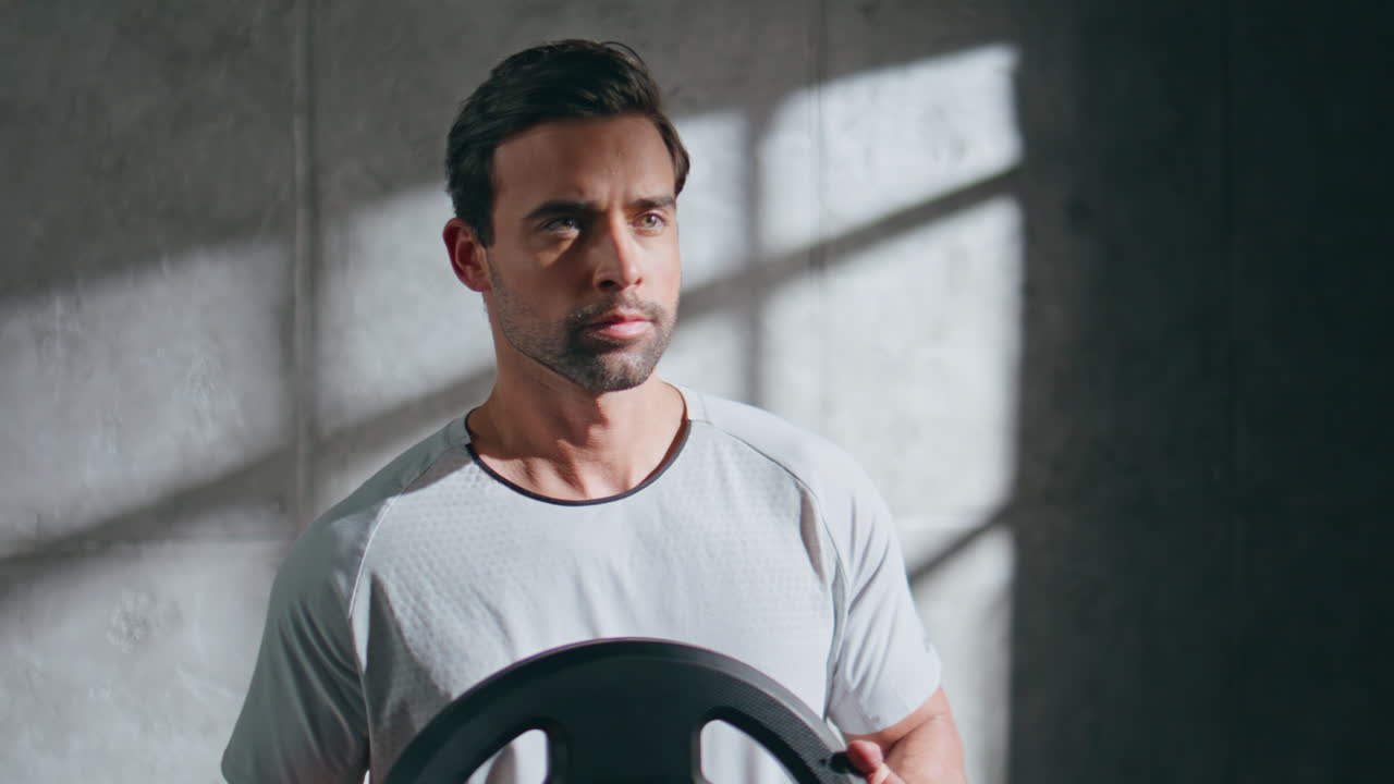 Strong powerlifter holding weights in loft gym closeup. Man rotating with plate