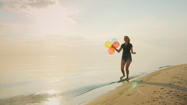 Carefree Young Woman Running On The Beach Holding Balloons In His Hand Concept - The Ease Freedom Jo