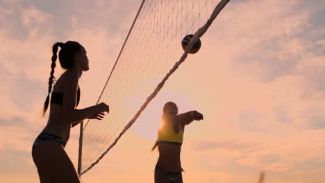 slow motion low angle close up sun flare: athletic girl playing beach volleyball jumps in the air and strikes the ball over the net on a beautiful summer evening. caucasian woman score a point.