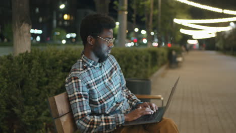 african american man using laptop in park in evening