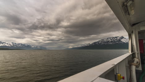 ferry travelling across vast ocean to oldervik-lyngen with a view of heavy clouds over snowy mountains in northern norway