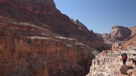 lonely female hiker with backpack in grand canyon national park walking on red rocks above abyss, slow motion