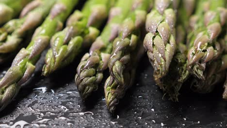 raw green asparagus on wet black slate background