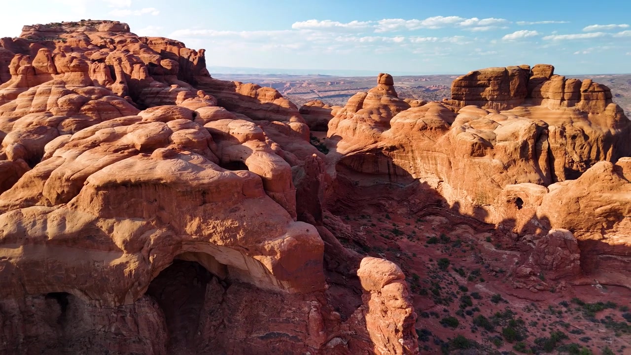 Splendido filmato stock del Parco Nazionale di Arches, USA, durante un pomeriggio luminoso. La luce solare brillante illumina le maestose strutture di arenaria rossa e il paesaggio desertico sotto un cielo azzurro limpido.