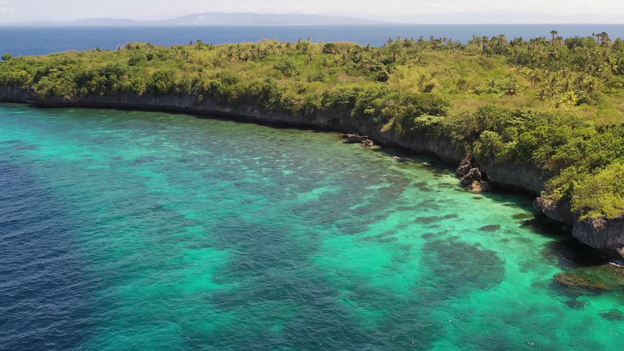 Overhead aerial view lowering down to clear turquoise water near tree lined shore