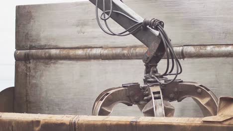 a hydraulic claw fetching a crushed car from inside a car crusher in a junkyard