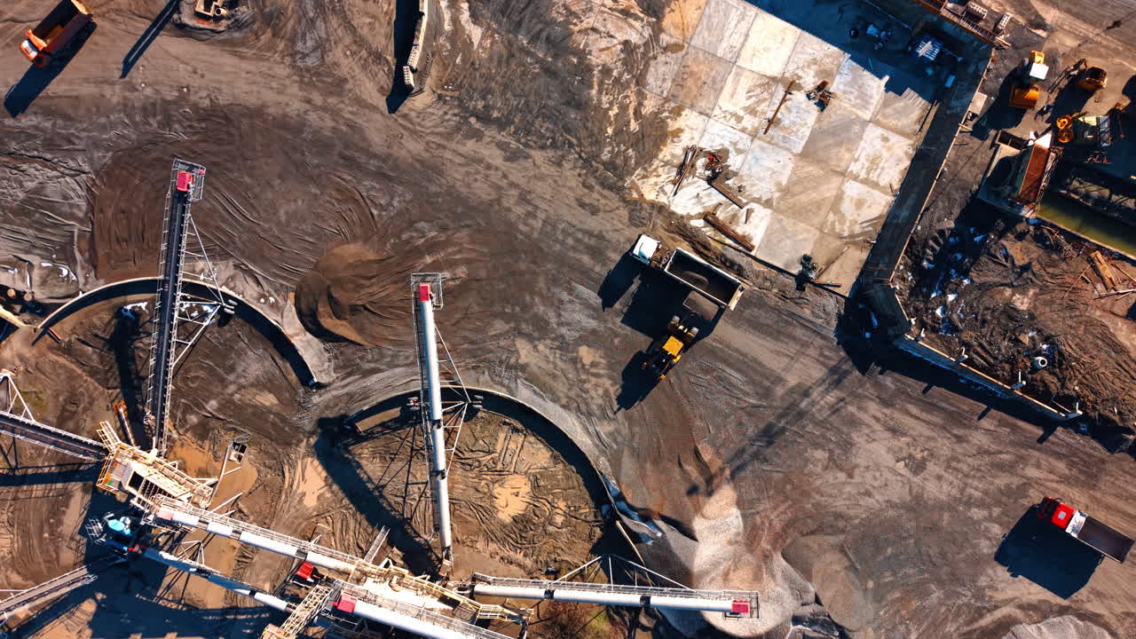 Industrial loader filling dump truck with stone at quarry. Aerial view of a front end loader loading a white truck in an industrial mining area