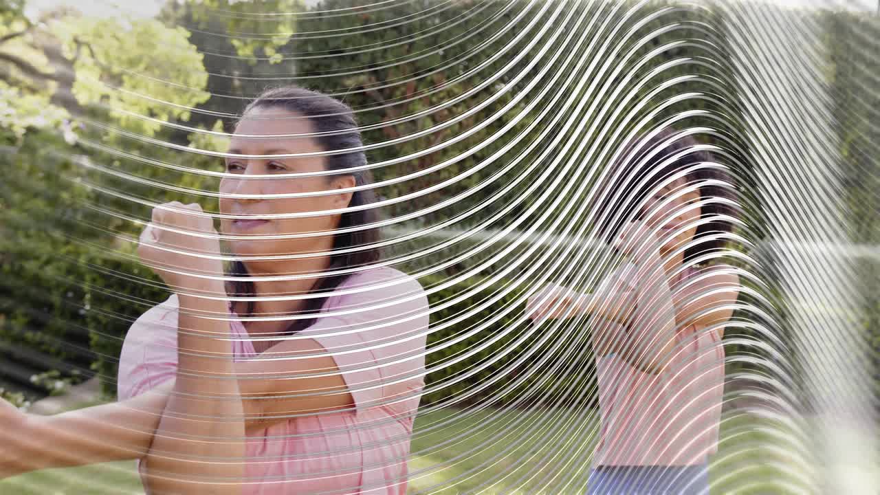 Two women mirroring wellness routine in yard lead lifting arms causing wavy overlay obscuring them